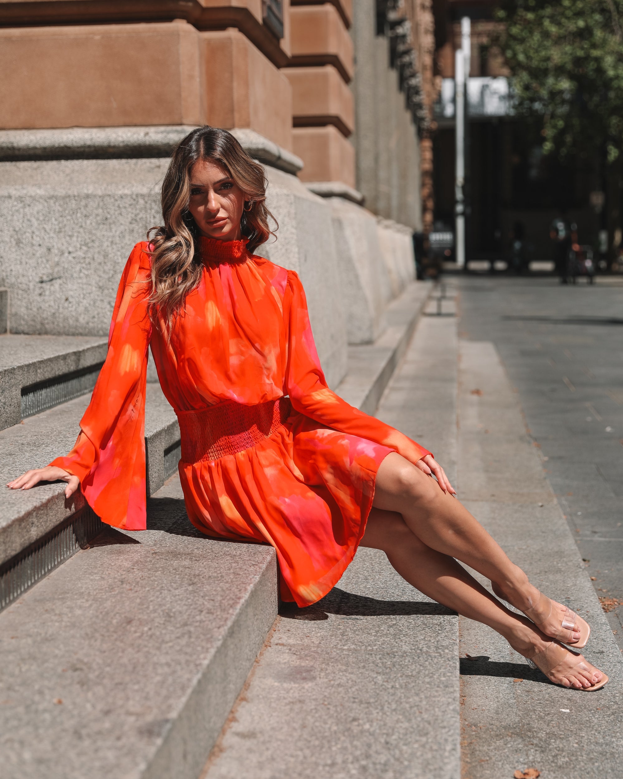 Model posing in the Daenerys Mini Dress Orange Print showing the flowing hem and long sleeve detail