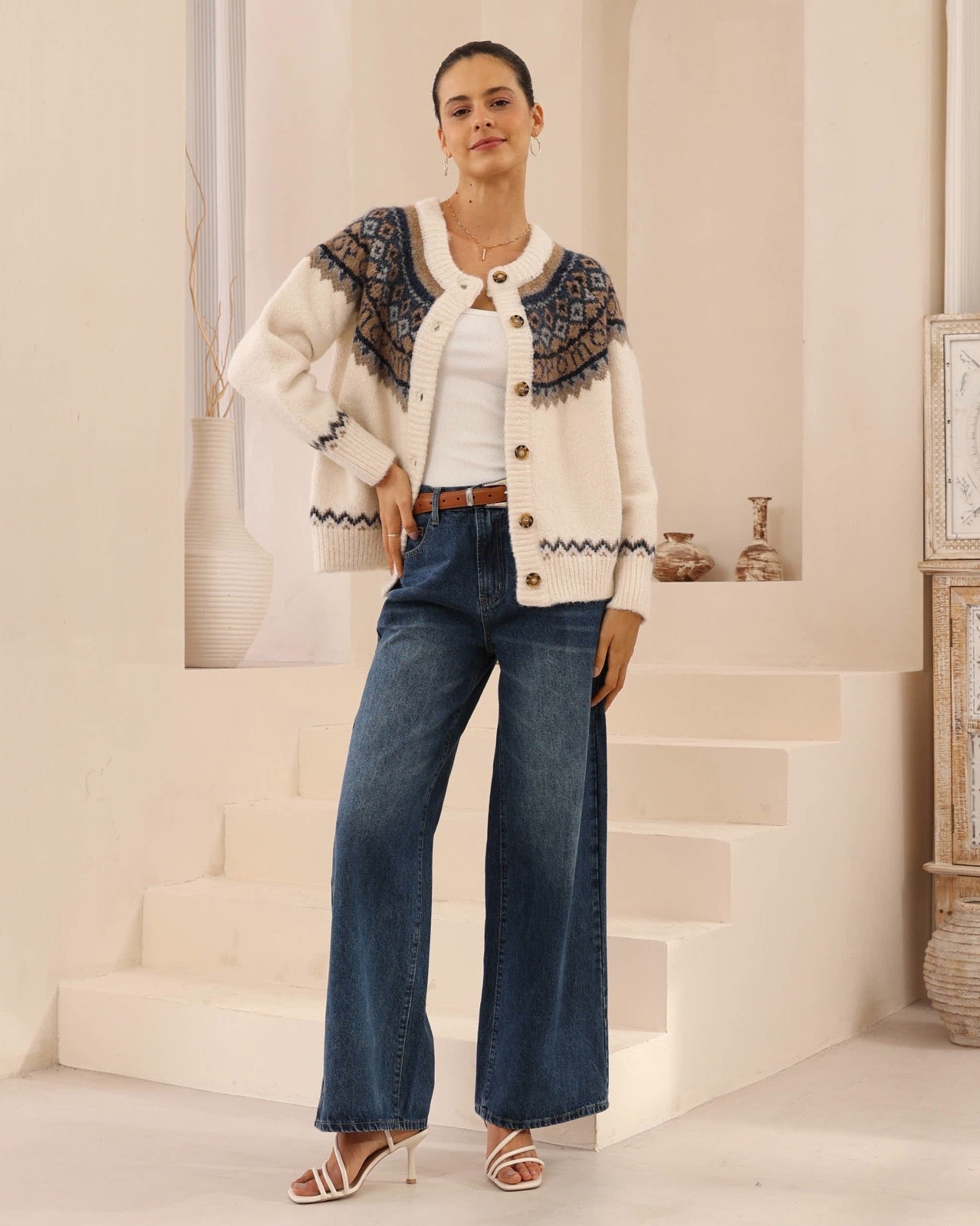 Woman wearing a patterned cardigan, white shirt, and blue jeans in an indoor setting.