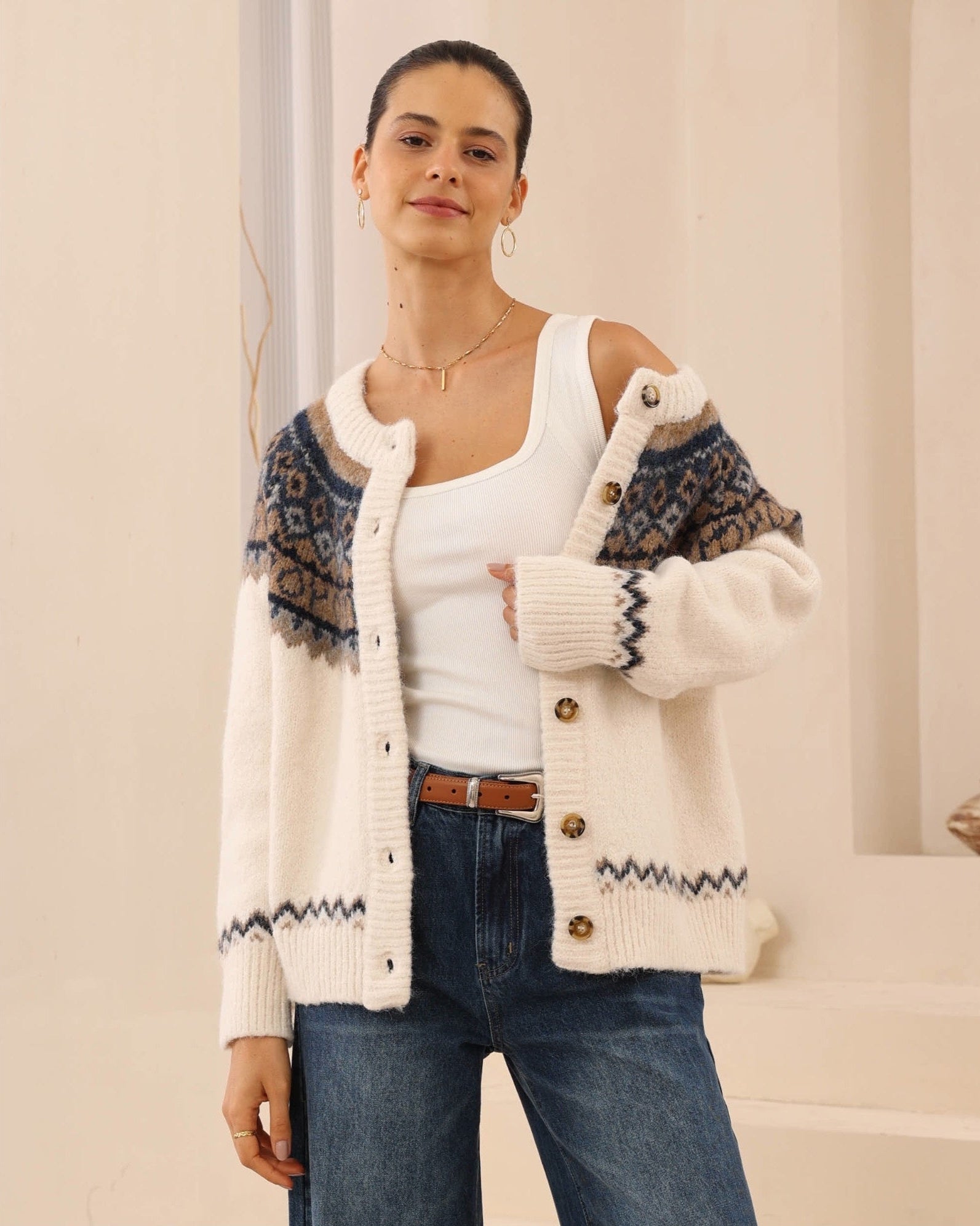 Woman wearing a patterned cardigan over a white top and blue jeans on a neutral background