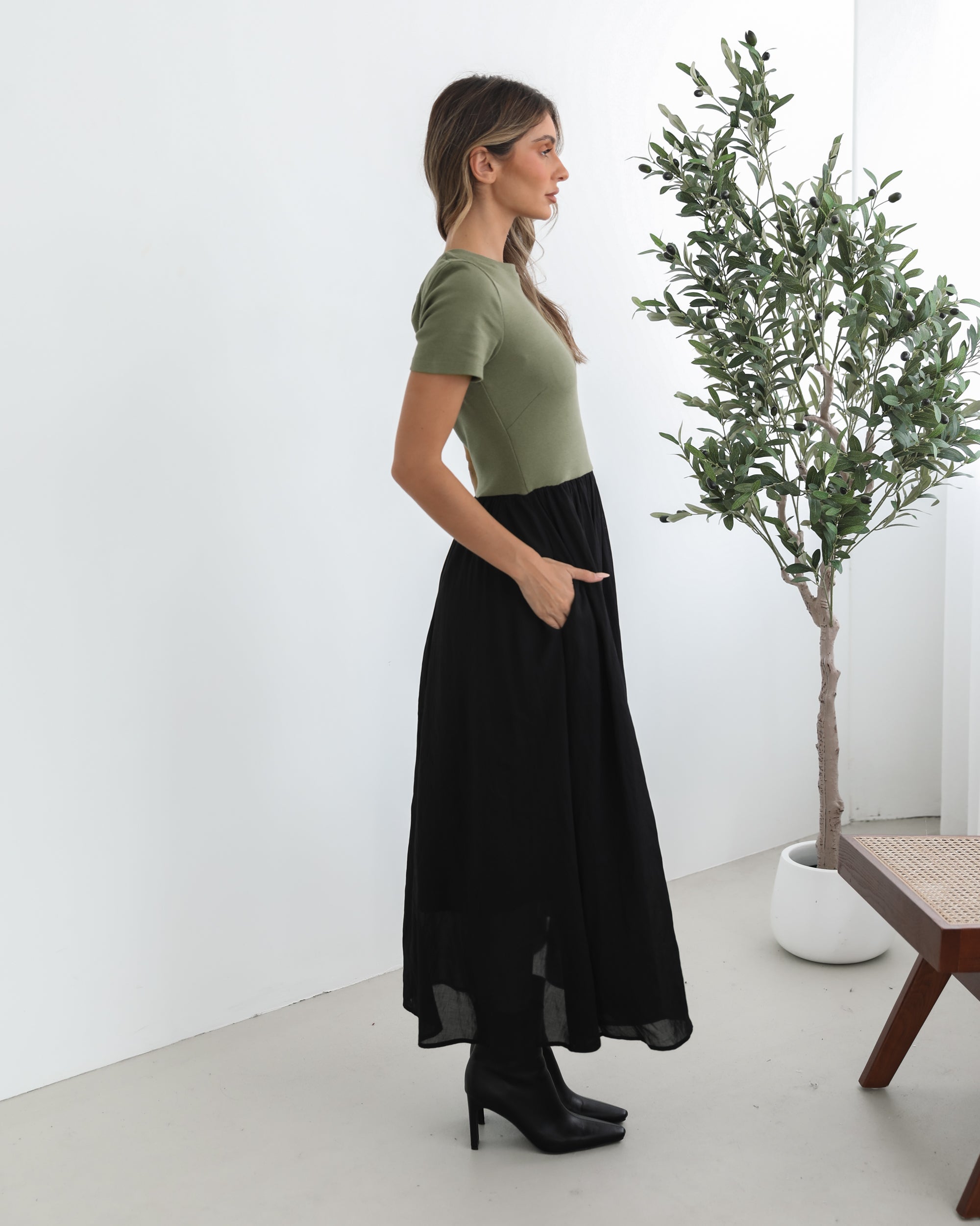 woman wearing a short sleeve round neck dress with green top and black flowy skirt paired with black boots in a white background studio