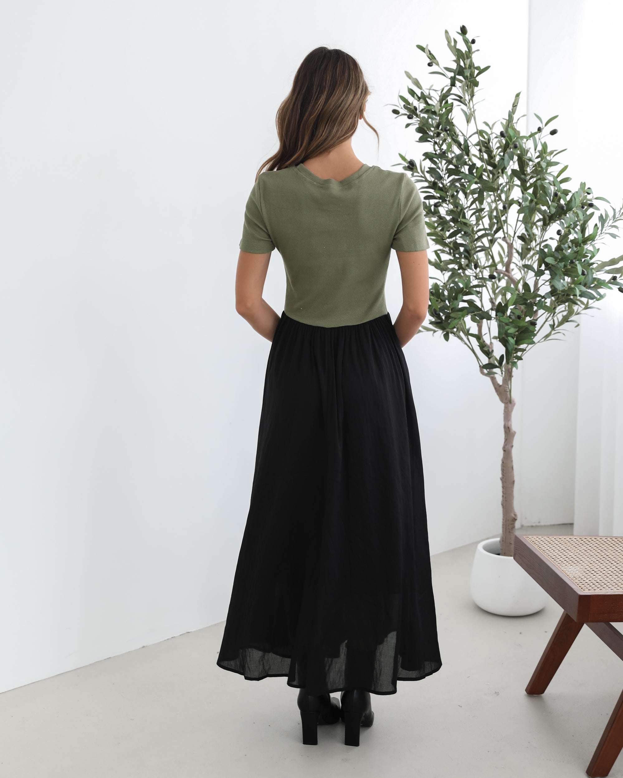woman wearing a short sleeve round neck dress with green top and black flowy skirt paired with black boots in a white background studio
