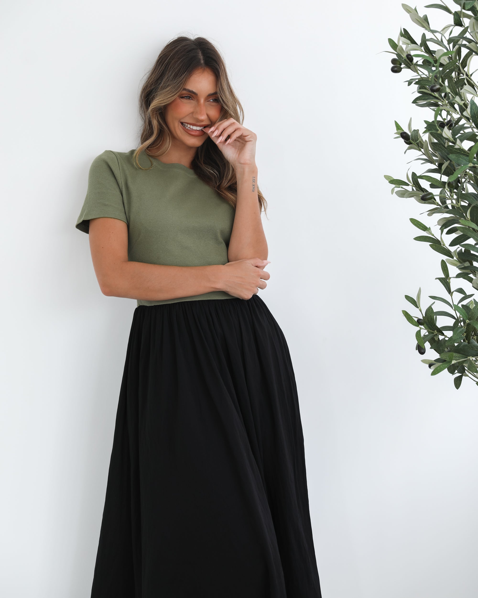 woman wearing a short sleeve round neck dress with green top and black flowy skirt paired with black boots in a white background studio