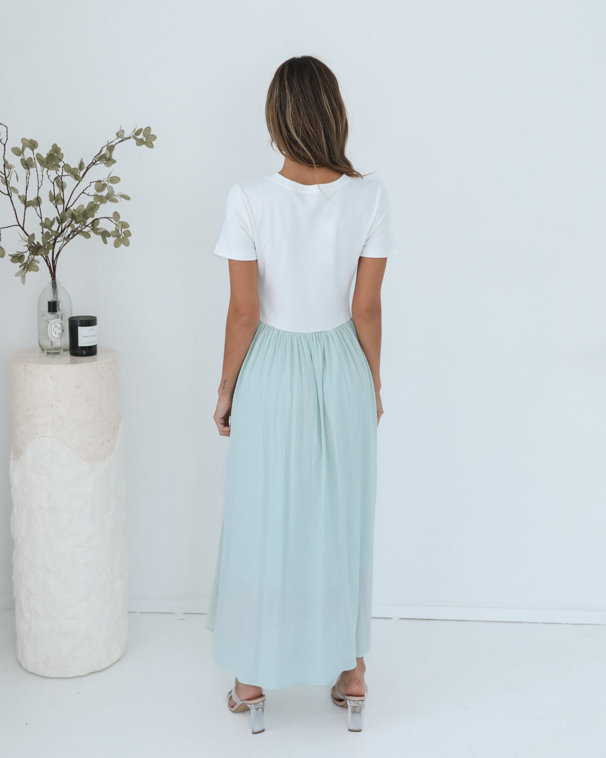 A woman wearing a knee-length dress with a round neckline and short sleeves. The dress is primarily white with sage green details.