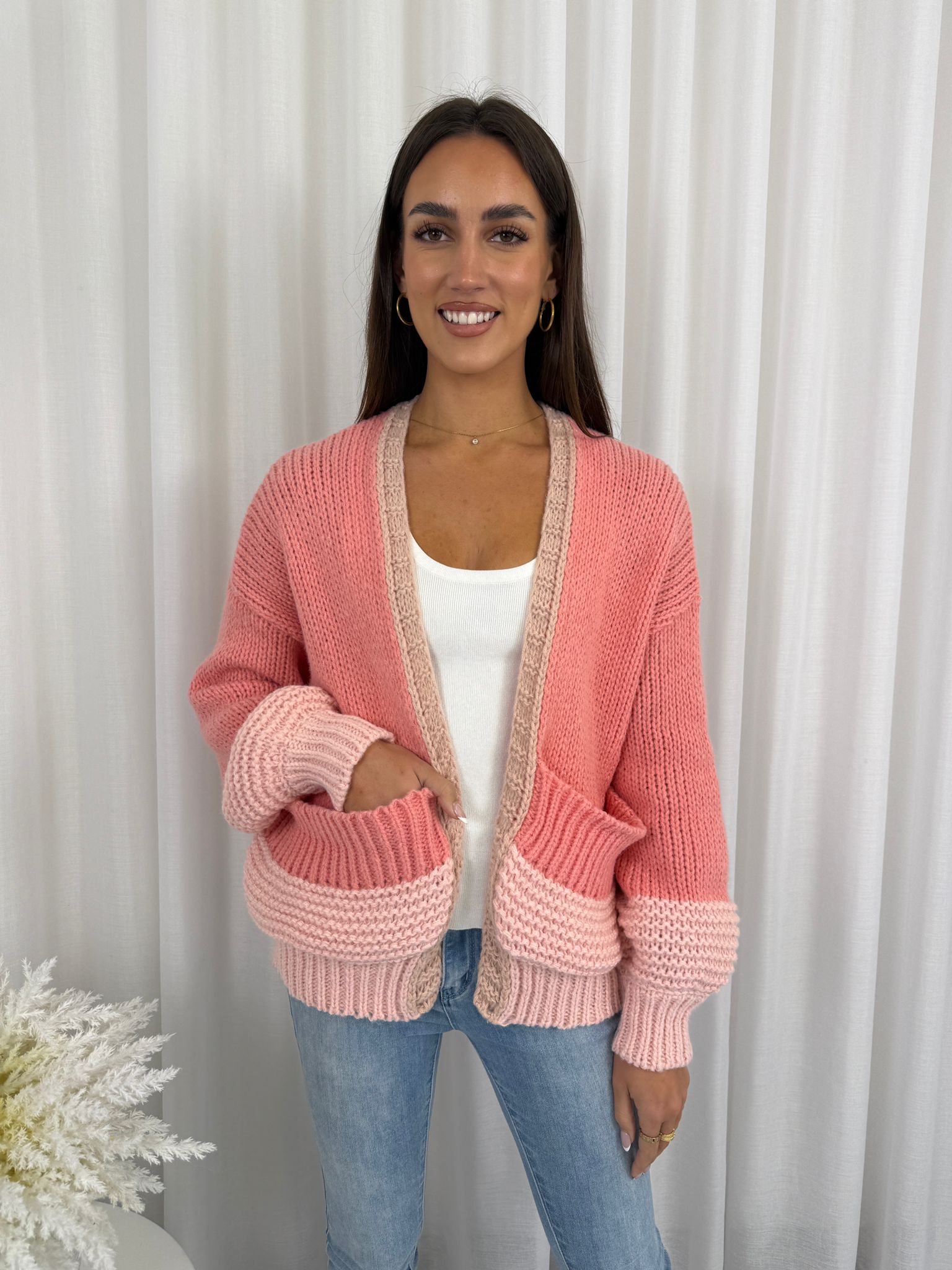 Woman wearing a pink knitted cardigan against a white curtain background