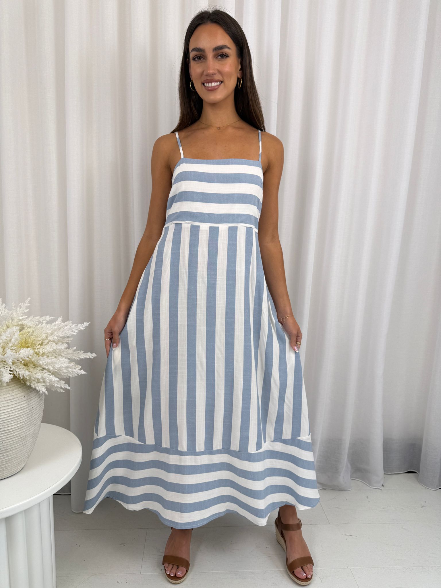 Woman wearing a blue and white striped dress against a white curtain background