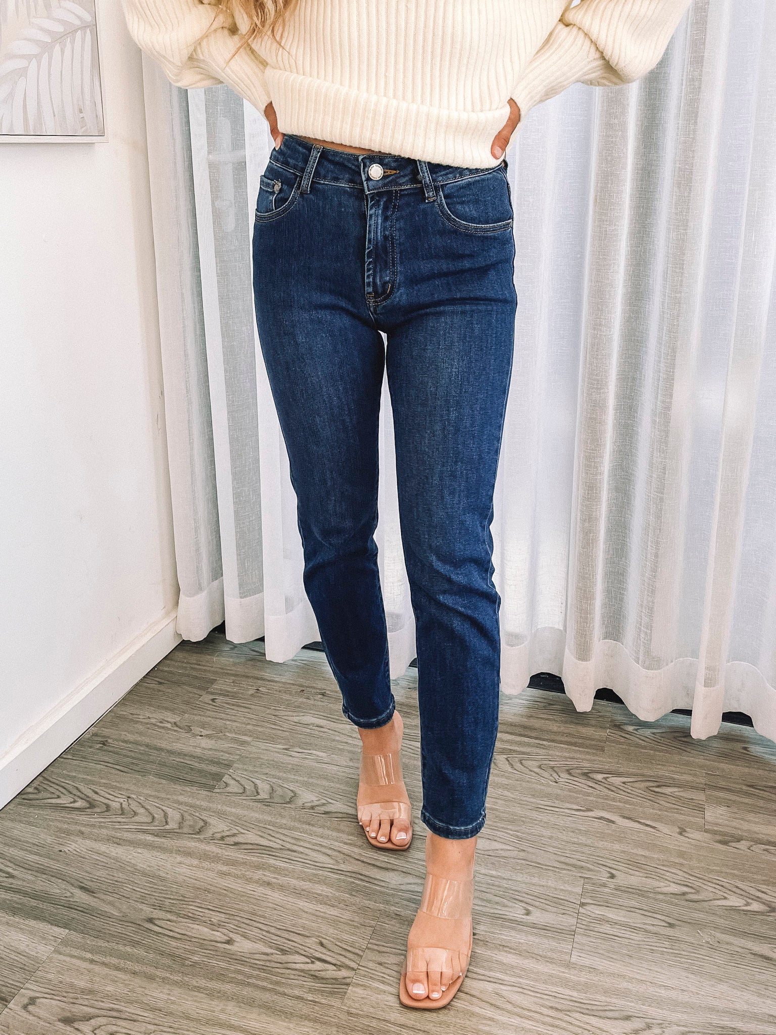 A person wearing a dark blue high-waisted, skinny fit pair of jeans with side pockets and a button and quarter zip closure.