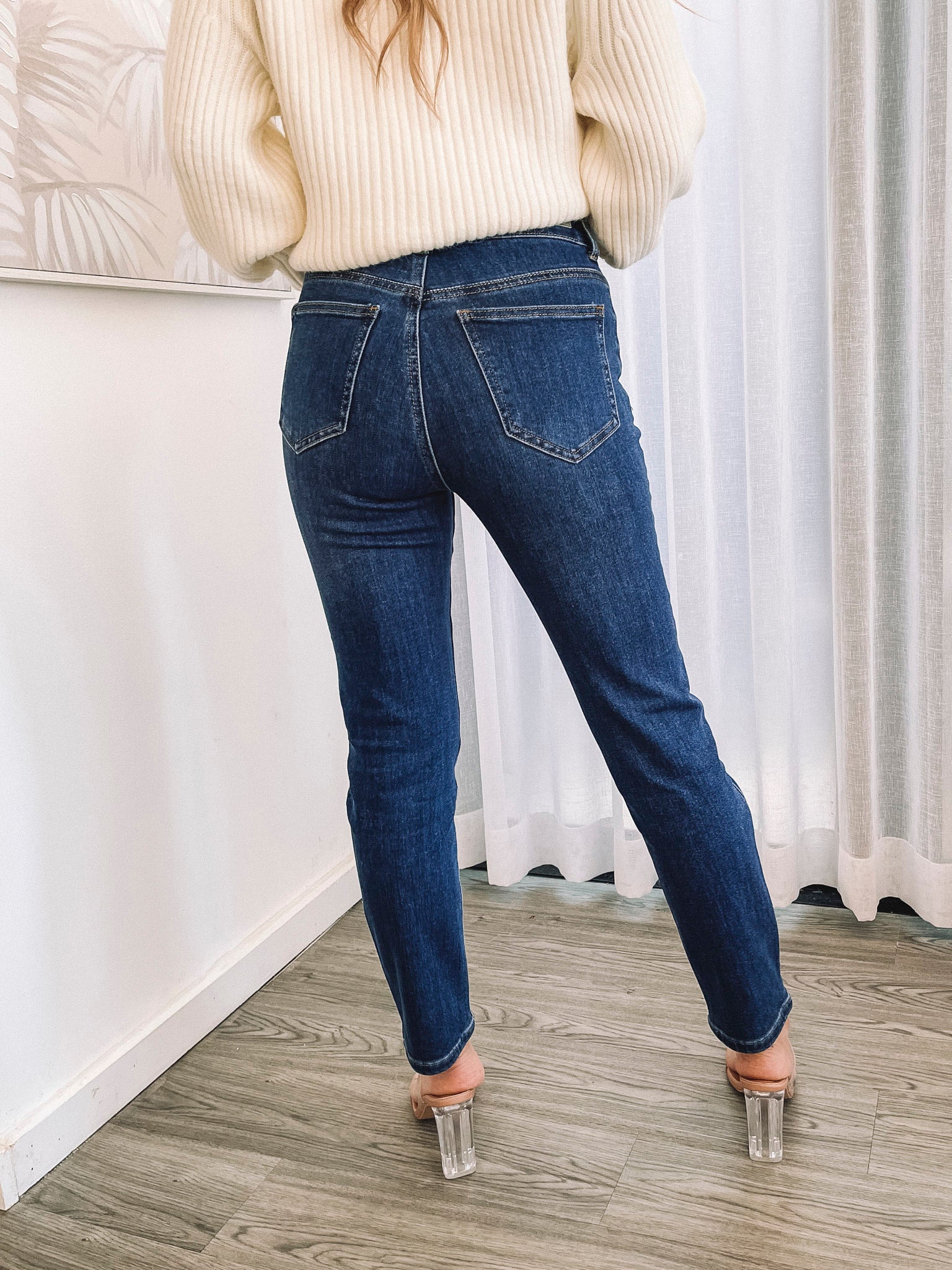 A person wearing a dark blue high-waisted, skinny fit pair of jeans with side pockets and a button and quarter zip closure.