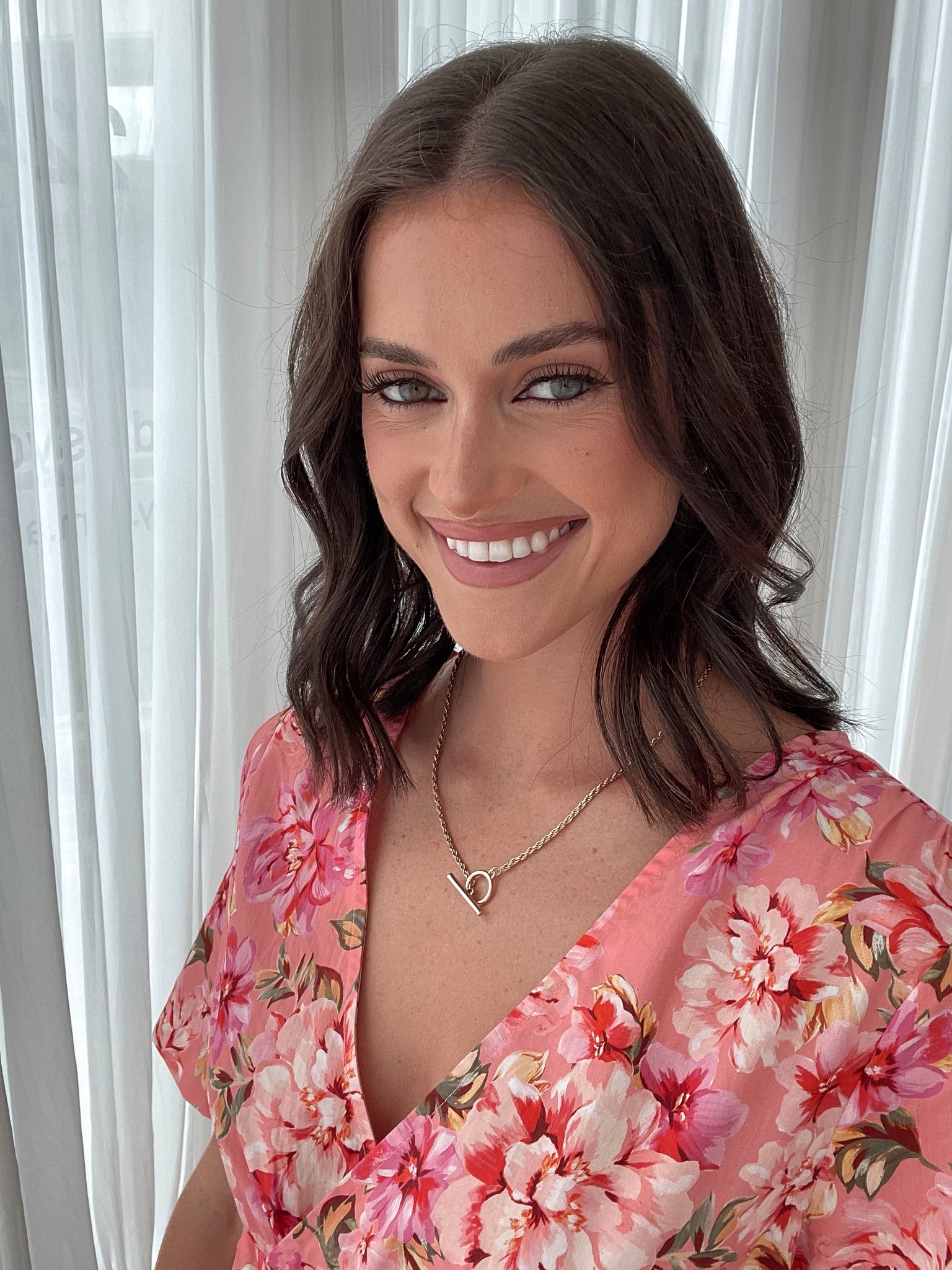 A person sitting on a white sofa wearing a peach blossom midi dress with a wide v-neckline, short puff sleeves, and a flowy a-line skirt.