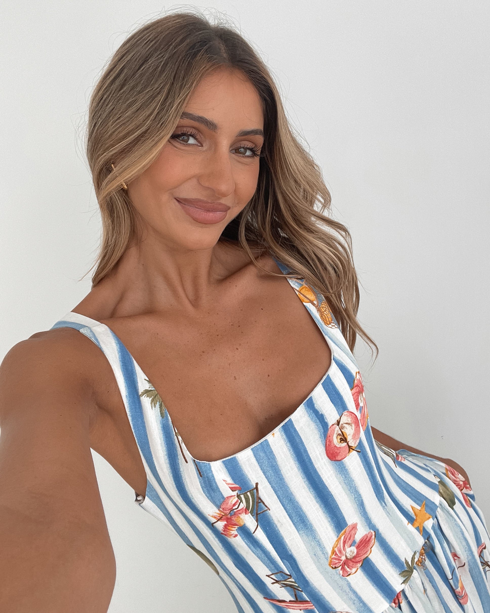 A model wearing a white and blue base multicolored print maxi dress with a square neckline and wide straps.