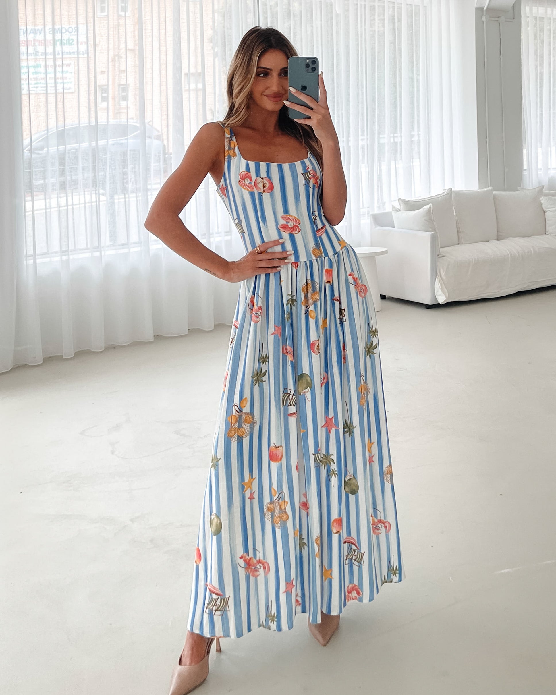 A model wearing a white and blue base multicolored print maxi dress with a square neckline and wide straps.