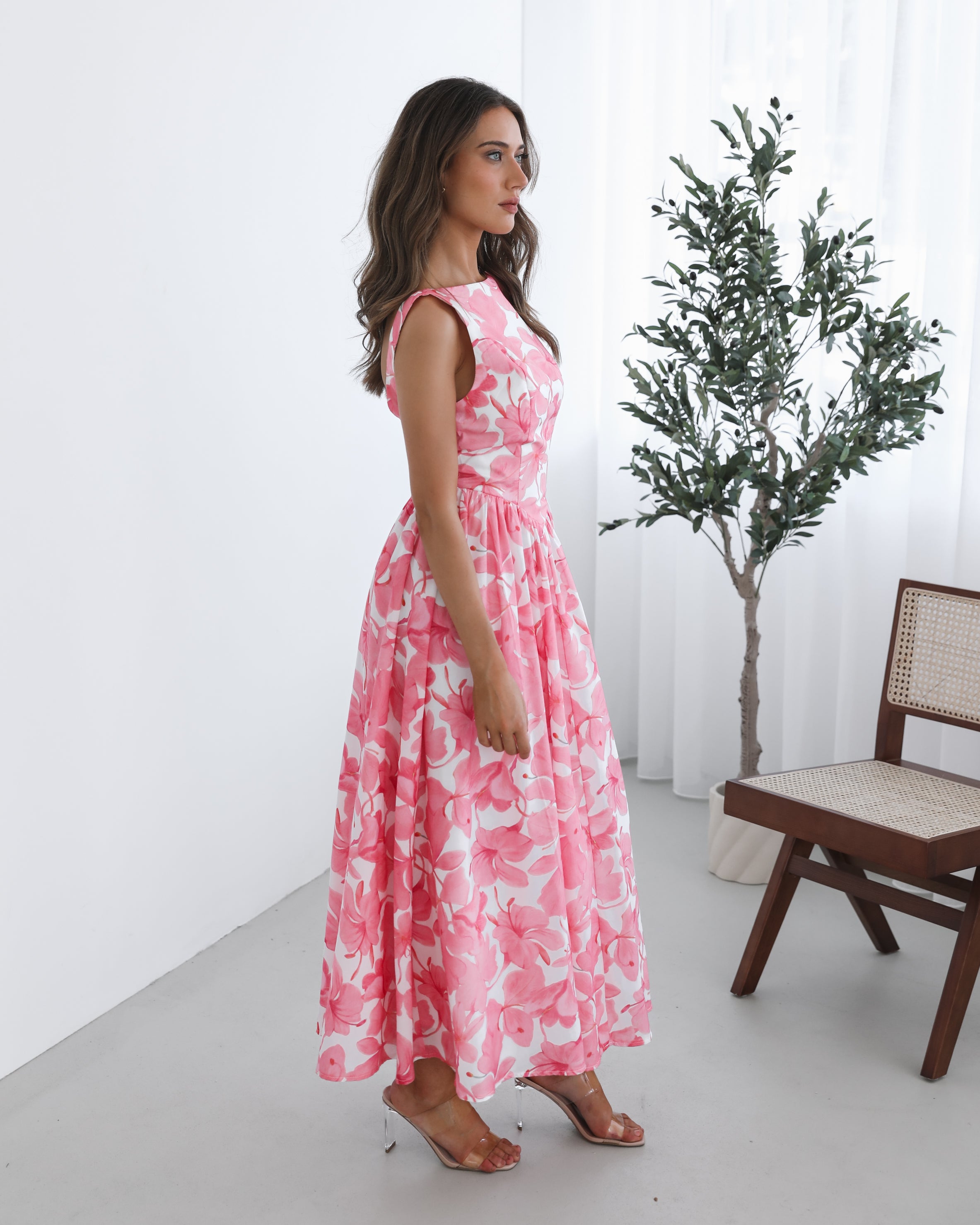 A woman wearing a pink floral maxi dress with a boat neckline and a flowy skirt.