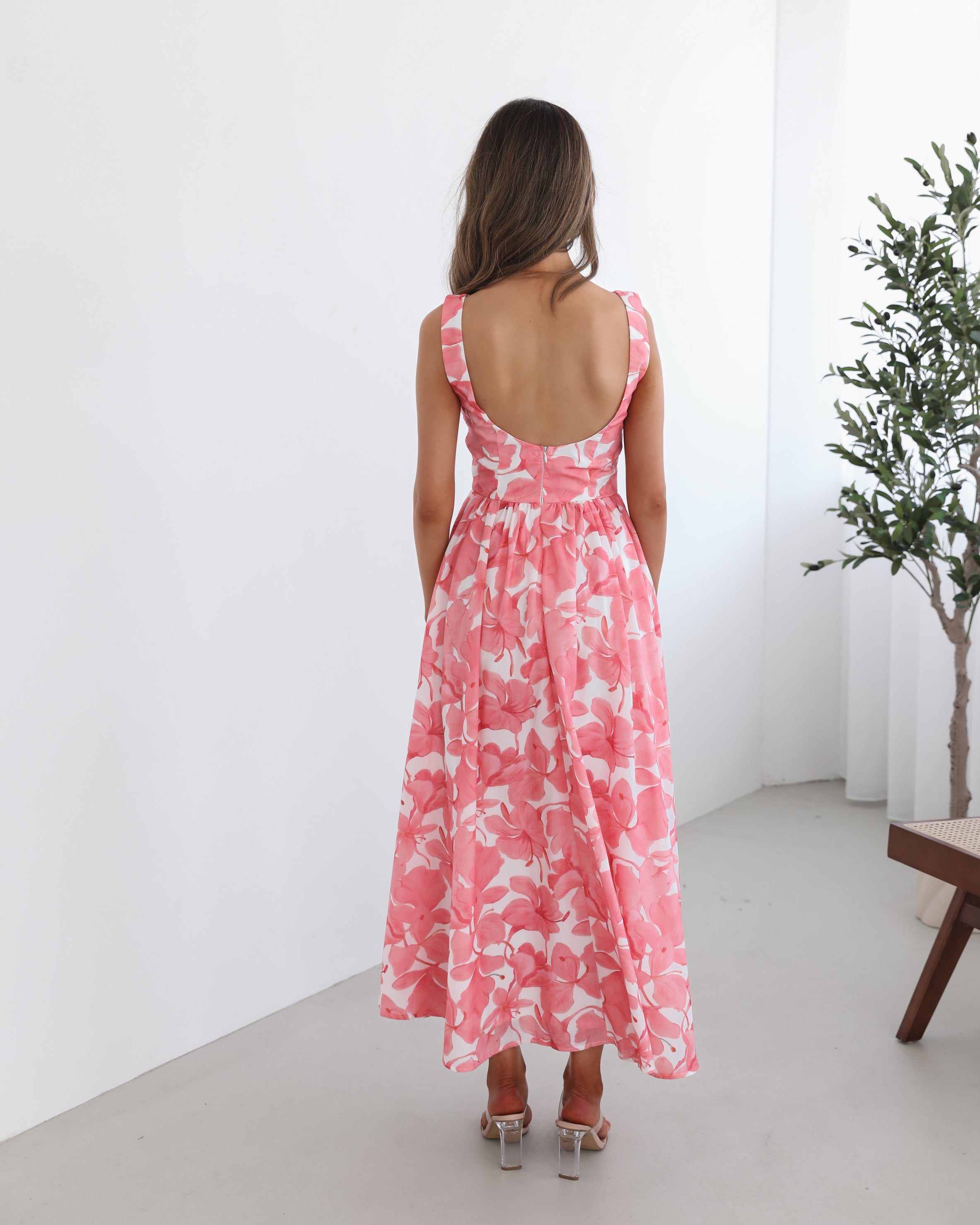 A woman wearing a pink floral maxi dress with a boat neckline and a flowy skirt.
