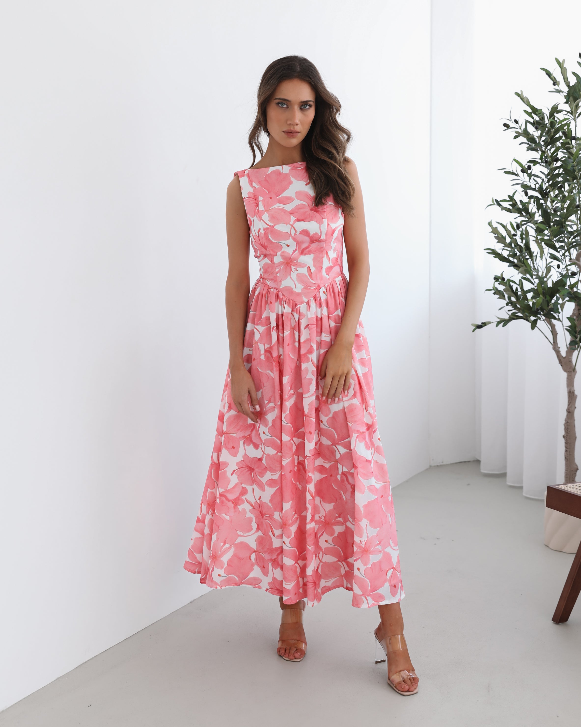 A woman wearing a pink floral maxi dress with a boat neckline and a flowy skirt.