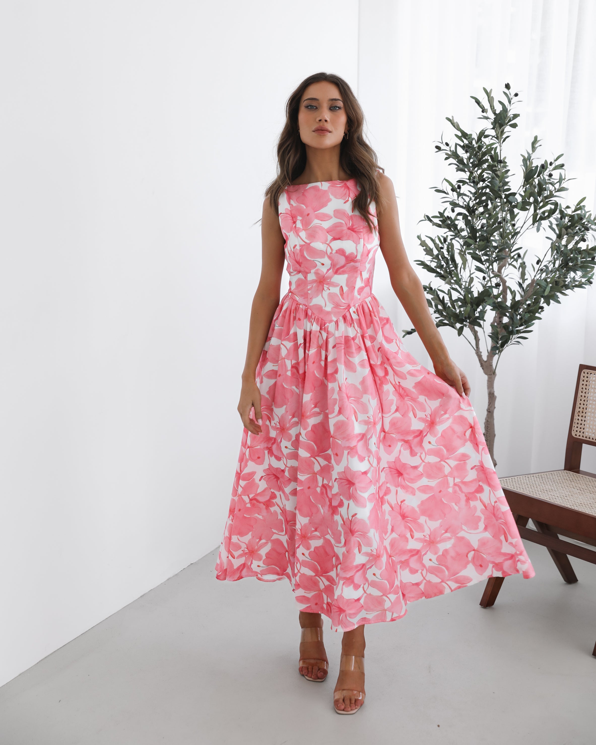A woman wearing a pink floral maxi dress with a boat neckline and a flowy skirt.
