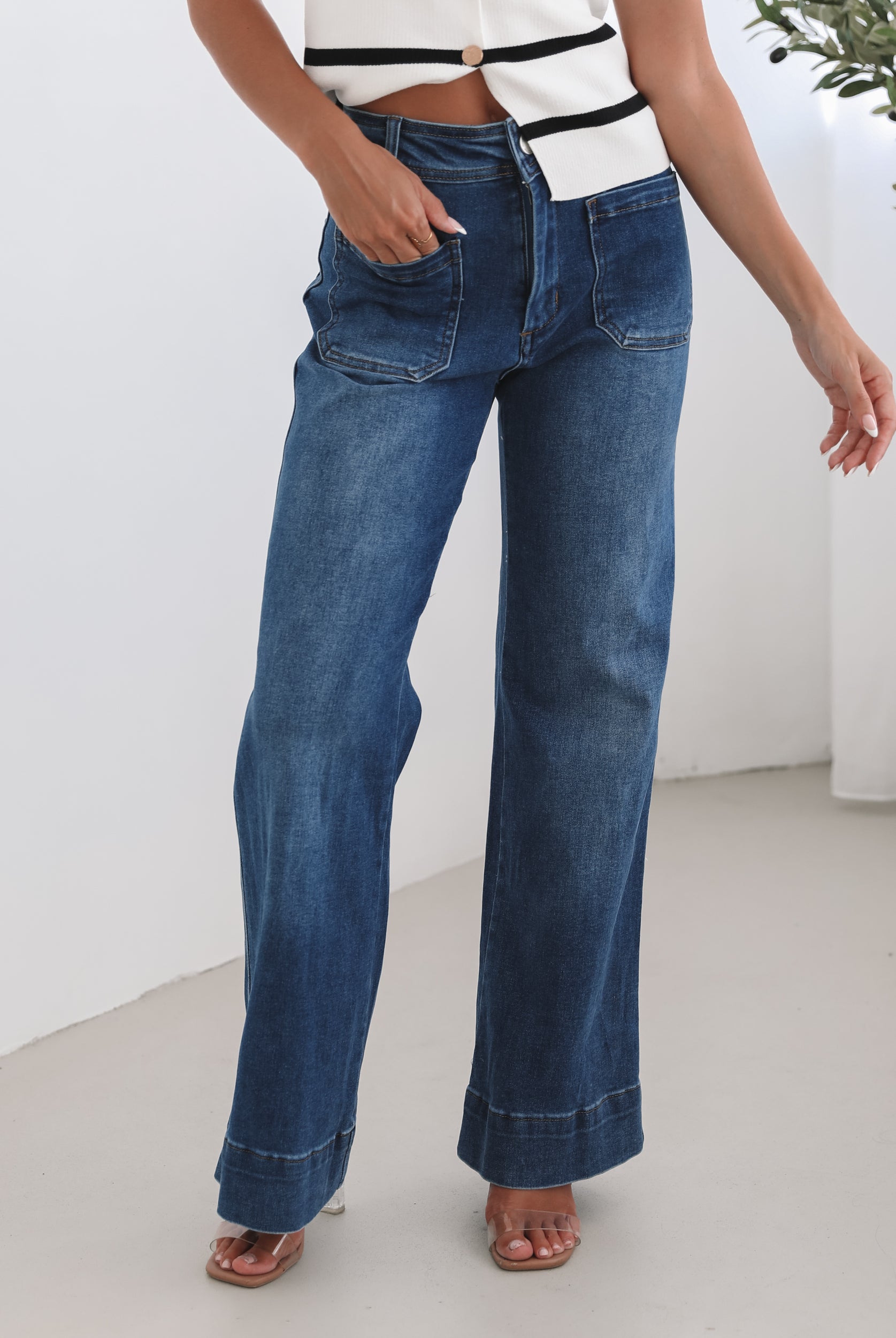 A woman standing in a room with light decor, wearing a striped top and mid-blue Yzabel Jeans with a high waist fit and wide leg silhouette.