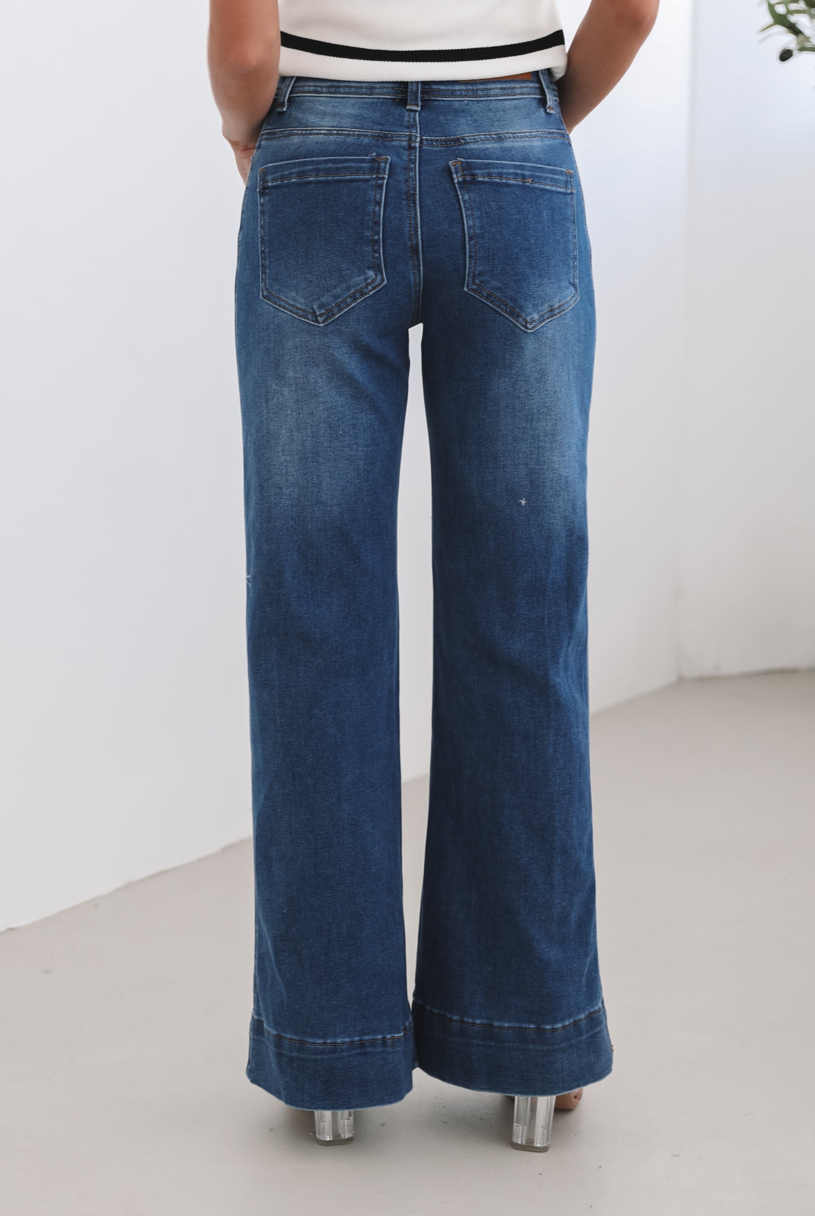 A woman standing in a room with light decor, wearing a striped top and mid-blue Yzabel Jeans with a high waist fit and wide leg silhouette.