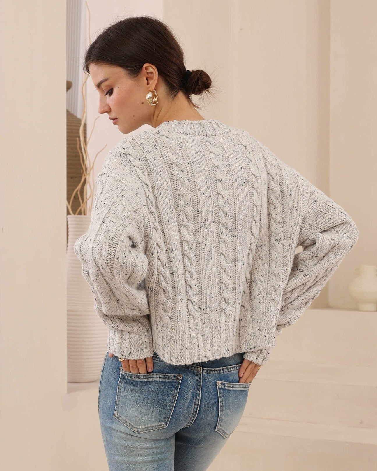 Woman wearing a cable knit sweater and jeans in a neutral setting