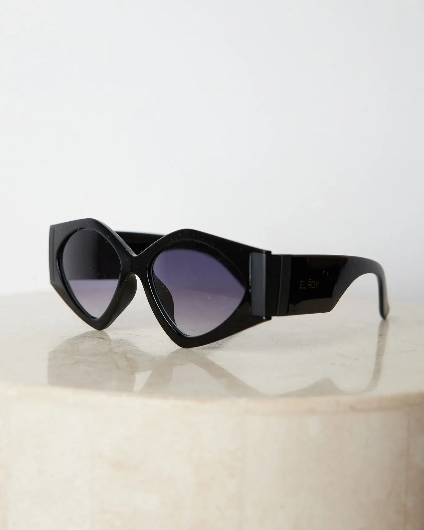Black cat-eye sunglasses with thick frames and dark tinted lenses, displayed on a light beige surface against a plain white background.