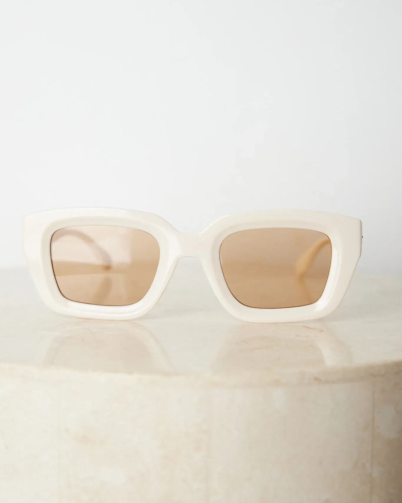 A pair of beige sunglasses displayed on a surface.