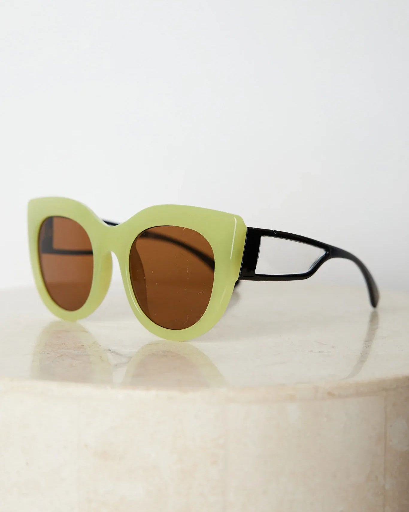 A pair of sunglasses with green frames and brown lenses displayed on a surface.