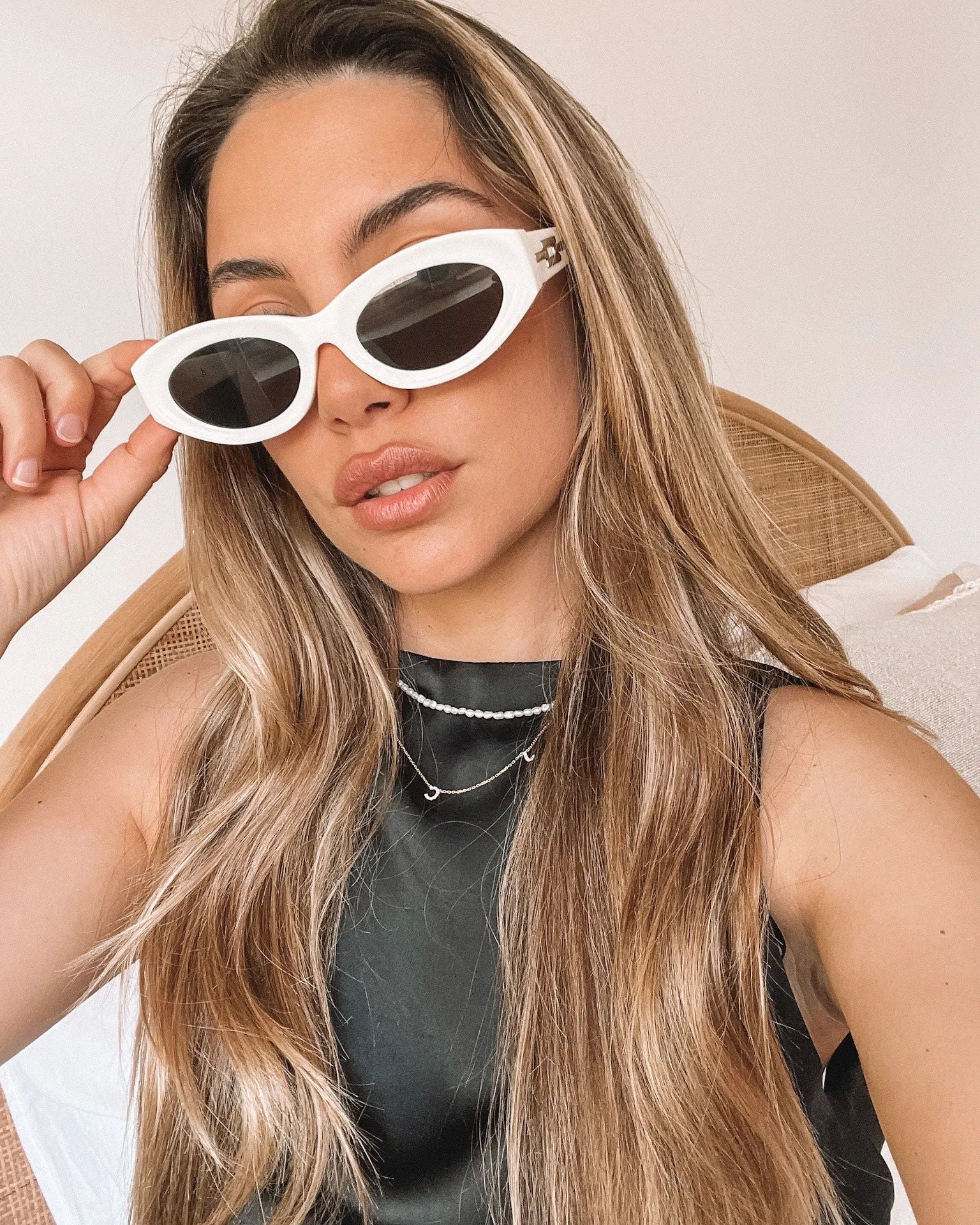 Close-up of a pair of white oval-shaped sunglasses with dark lenses, resting on a smooth beige surface against a plain white background.