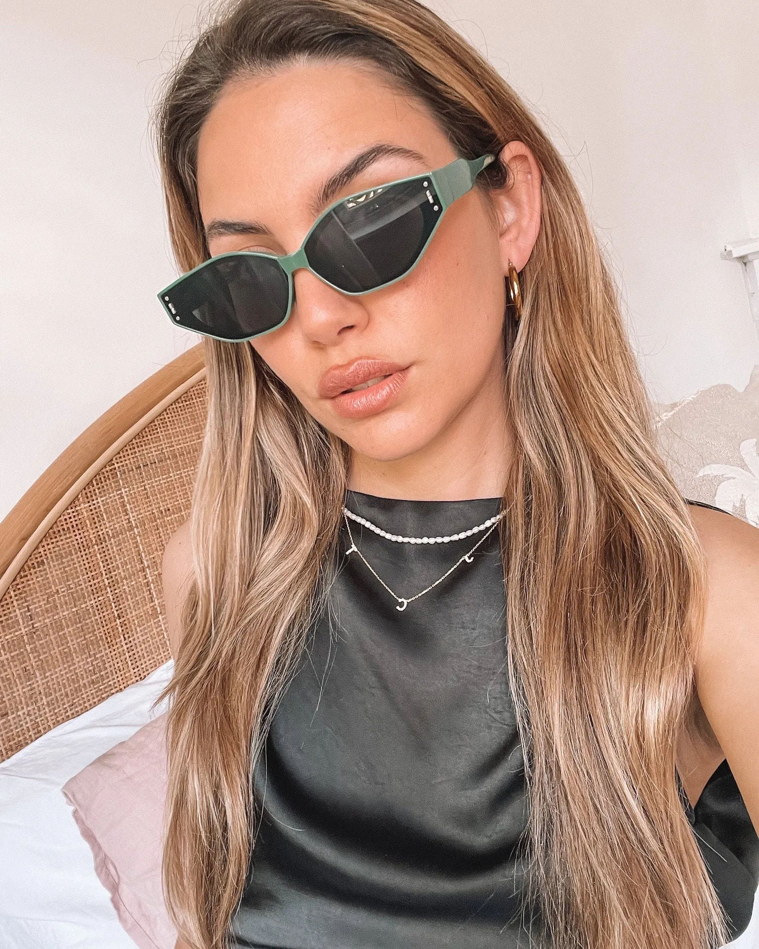 Green geometric-shaped sunglasses with dark lenses resting on a light marble surface against a plain white background.