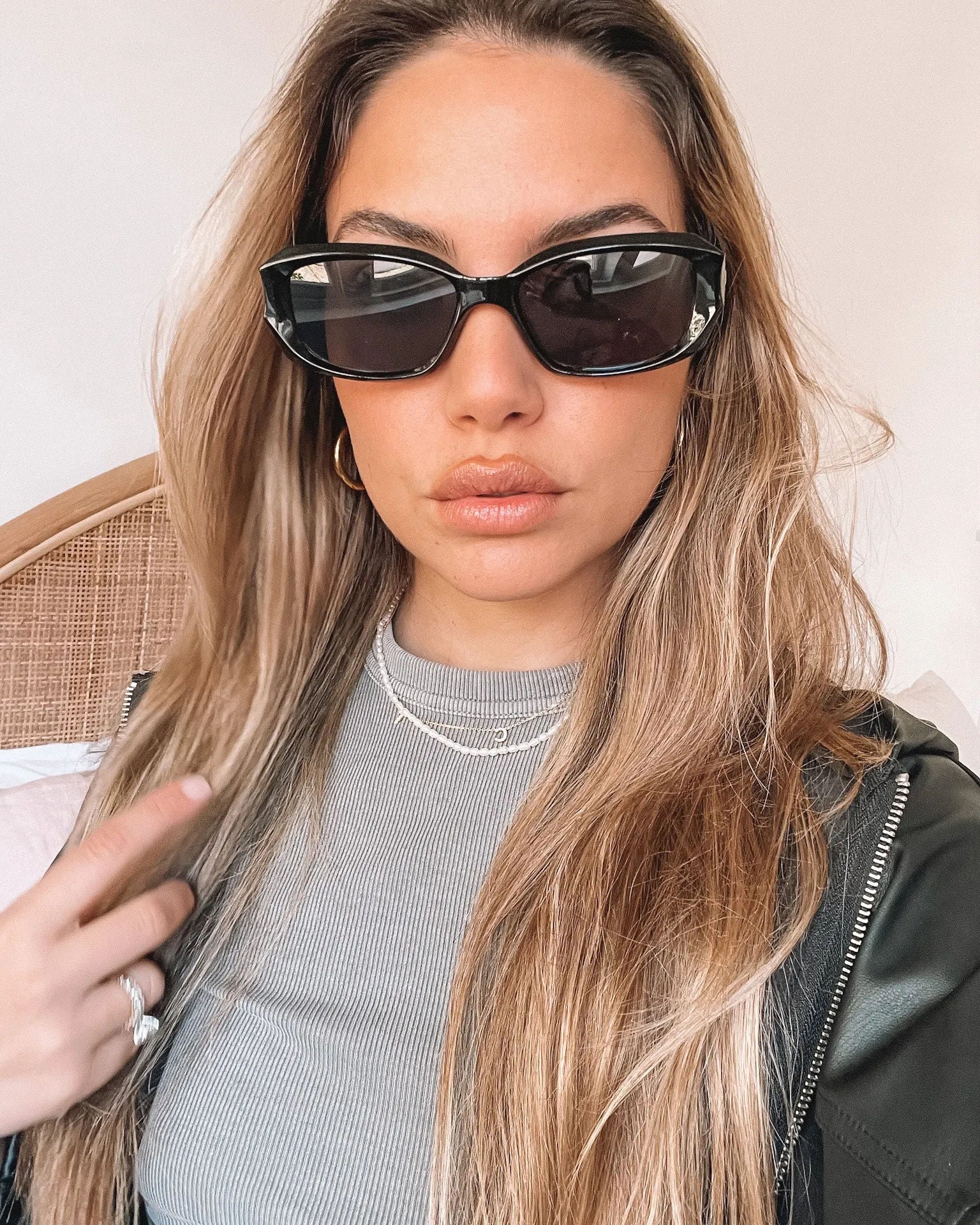 Black rectangular sunglasses with a glossy frame and dark tinted lenses, displayed on a light beige curved surface against a plain white background.