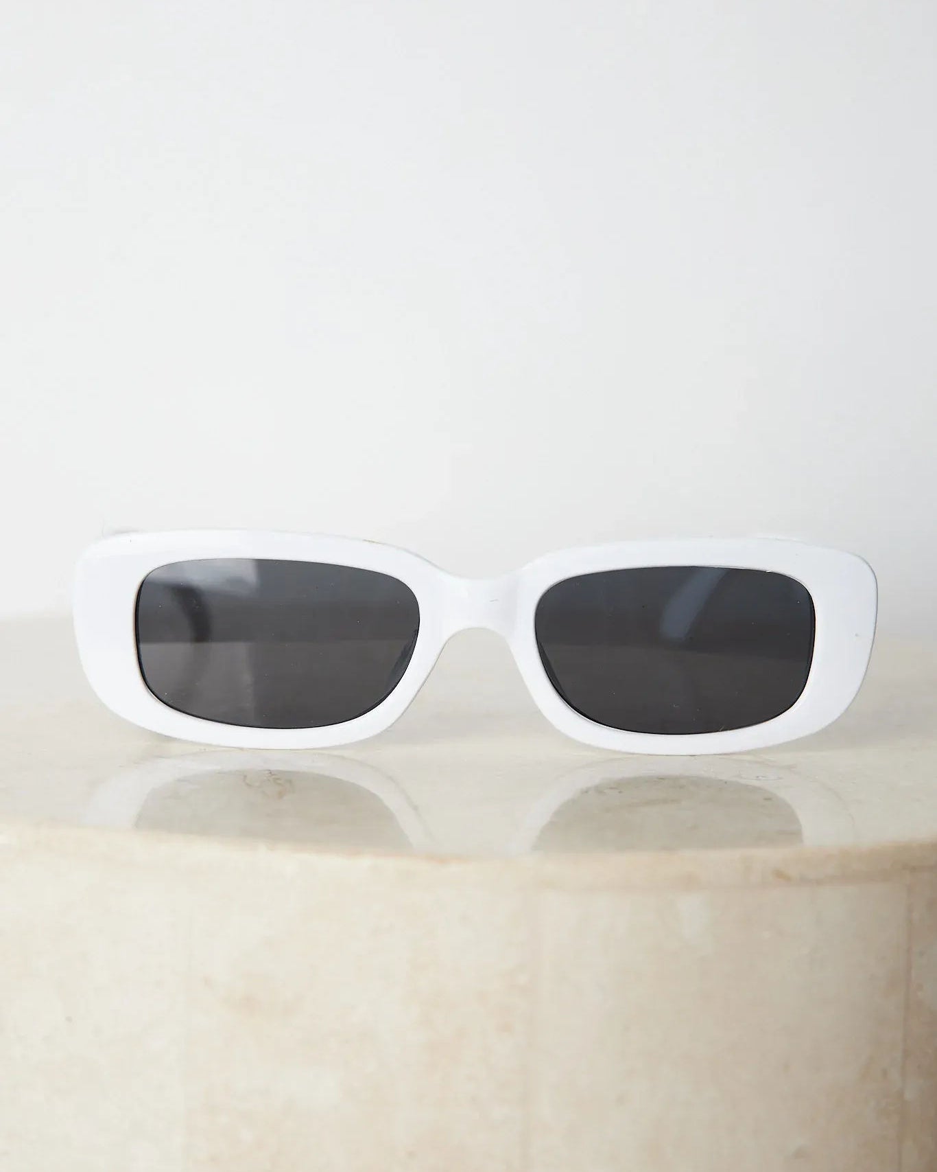A pair of white-framed sunglasses displayed against a neutral background.