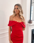 Elegant woman wearing a red off-shoulder gown, perfect for formal events, weddings, evening balls, and special occasions, standing in a sophisticated room with wooden flooring and a fireplace.