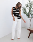A female model wearing white high-waisted jeans with brown contrasting stitches, paired with a striped black and white top.