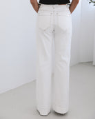 A female model wearing white high-waisted jeans with brown contrasting stitches, paired with a striped black and white top.