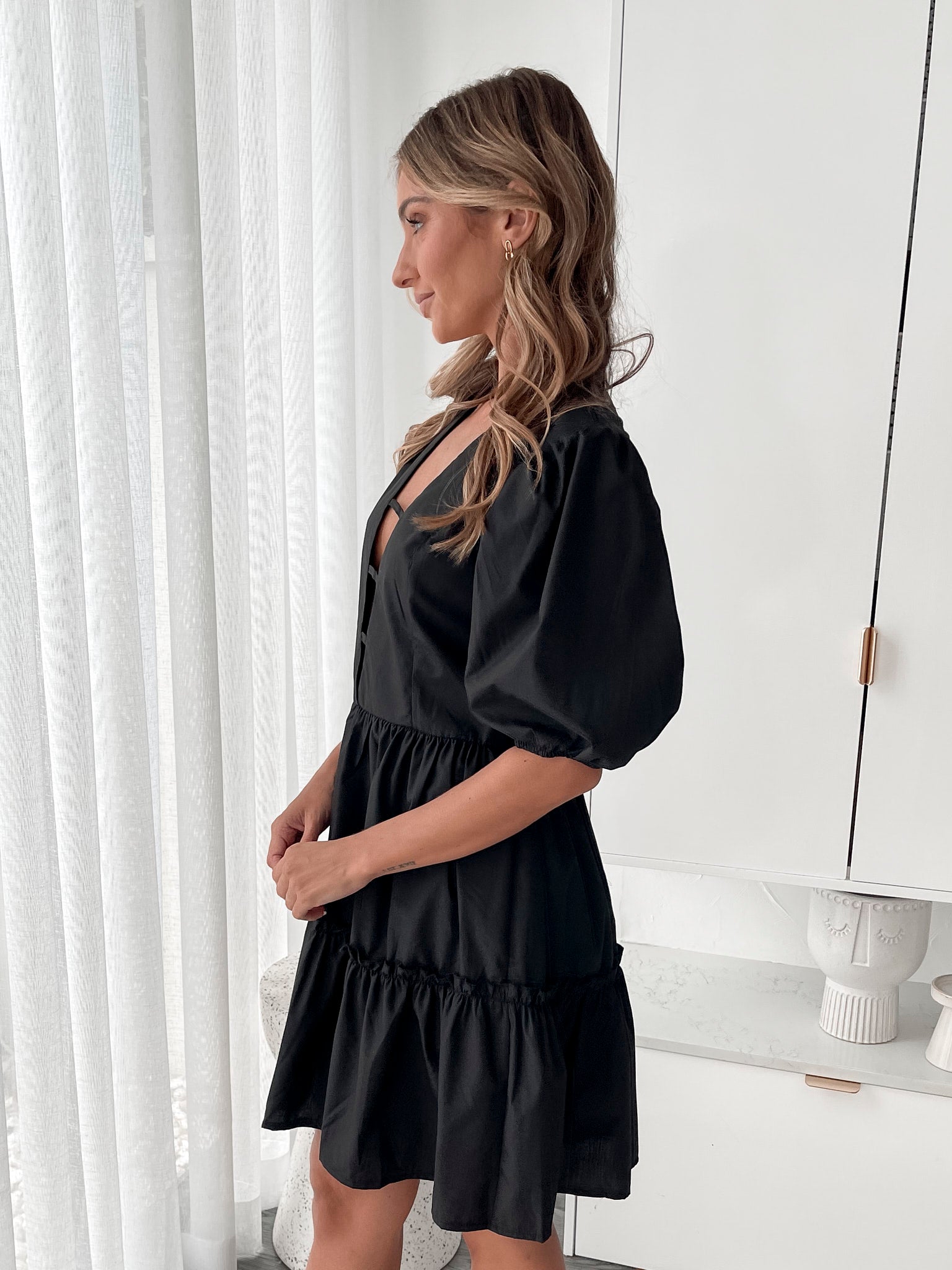 A woman wearing a classic black mini dress with a baby doll-inspired shape, featuring a plunge neckline and balloon sleeves.