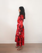 Woman wearing a red floral dress standing against a white wall.