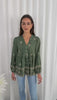 Woman wearing a green patterned blouse against a white curtain background