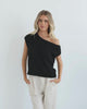 A female model wearing a black knit top with a one side off shoulder design, paired with light-colored trousers.
