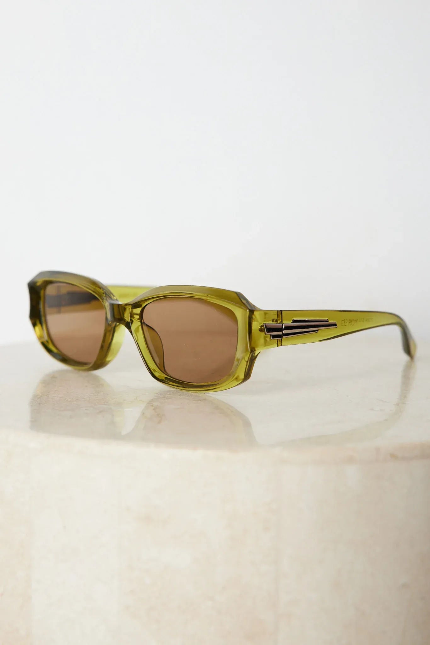 Rectangular sunglasses with translucent olive green frames and brown tinted lenses, displayed on a light beige stone surface against a plain white background.