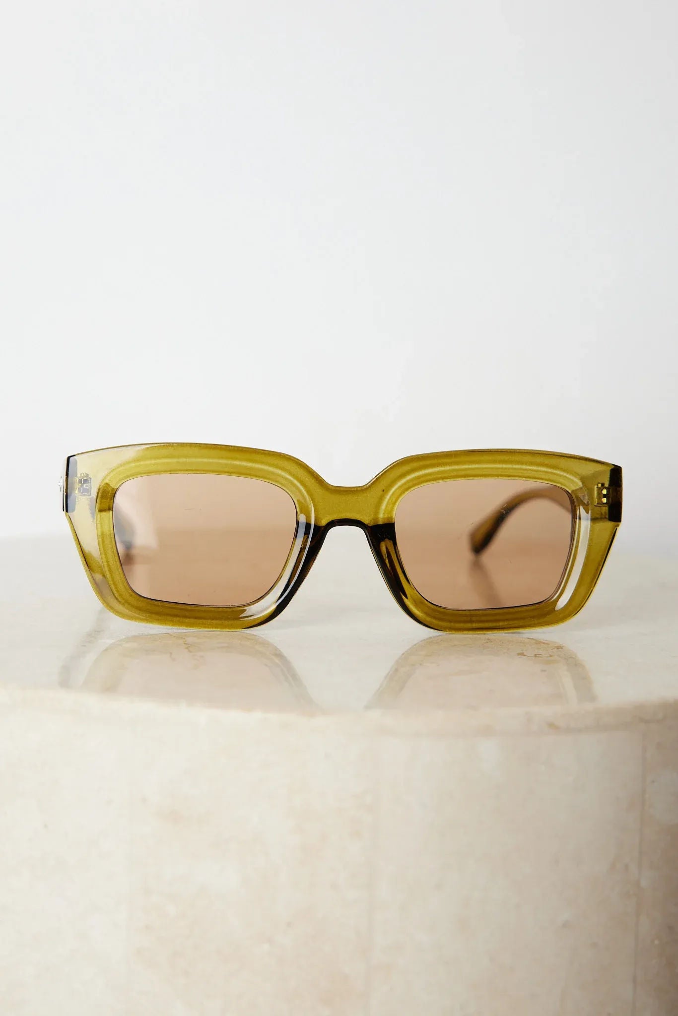 A pair of sunglasses with olive green frames and pink lenses displayed on a surface.