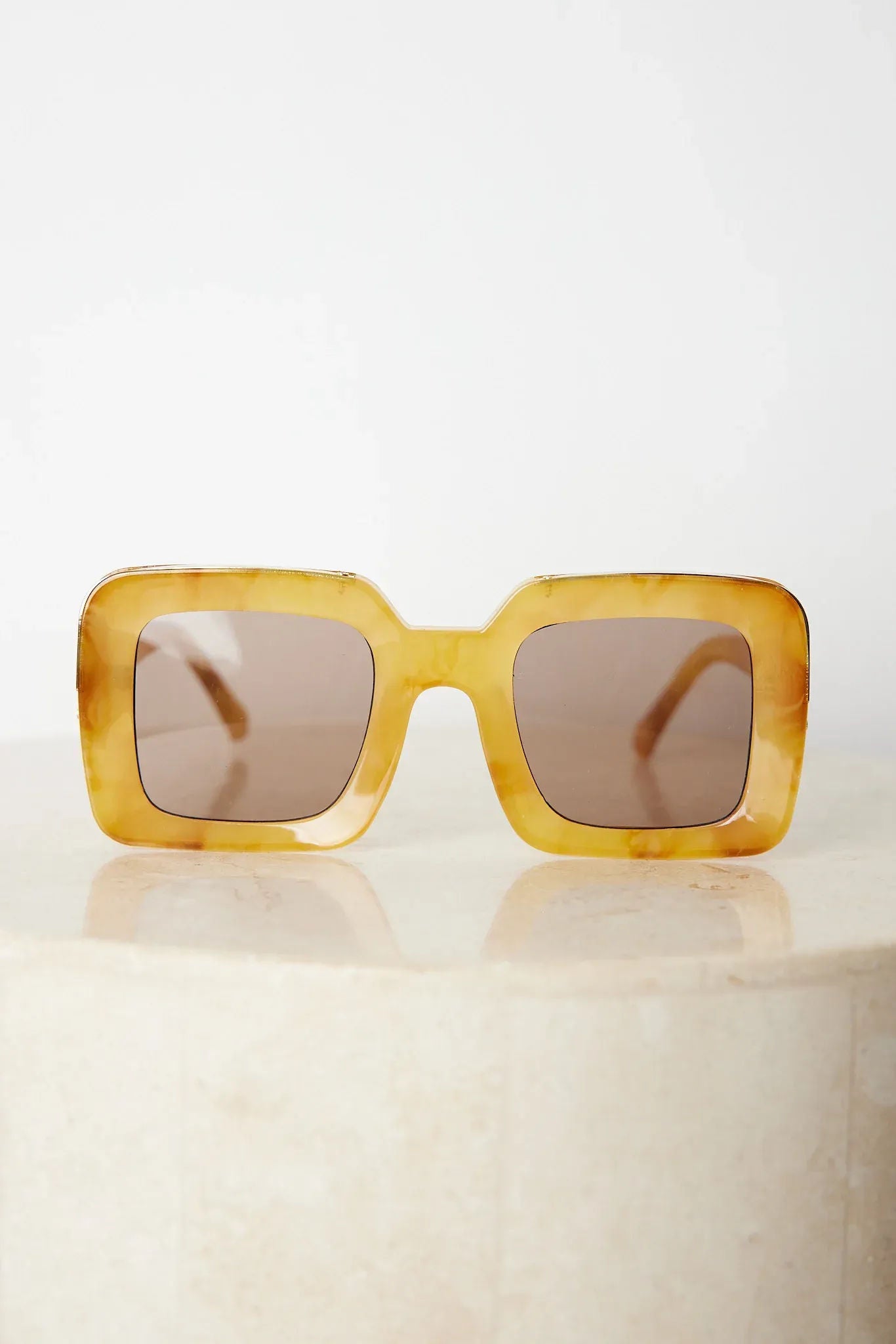 A pair of sunglasses with a tan frame displayed on a surface.